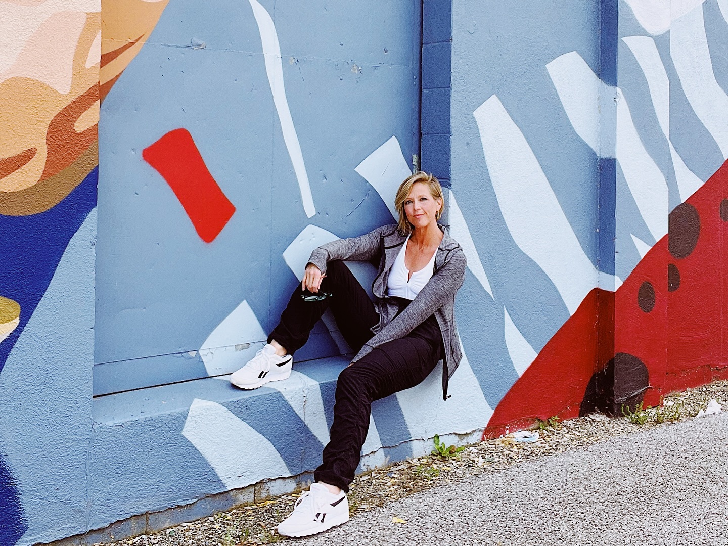 Woman in athletic wear sitting casually against a colorful abstract mural.