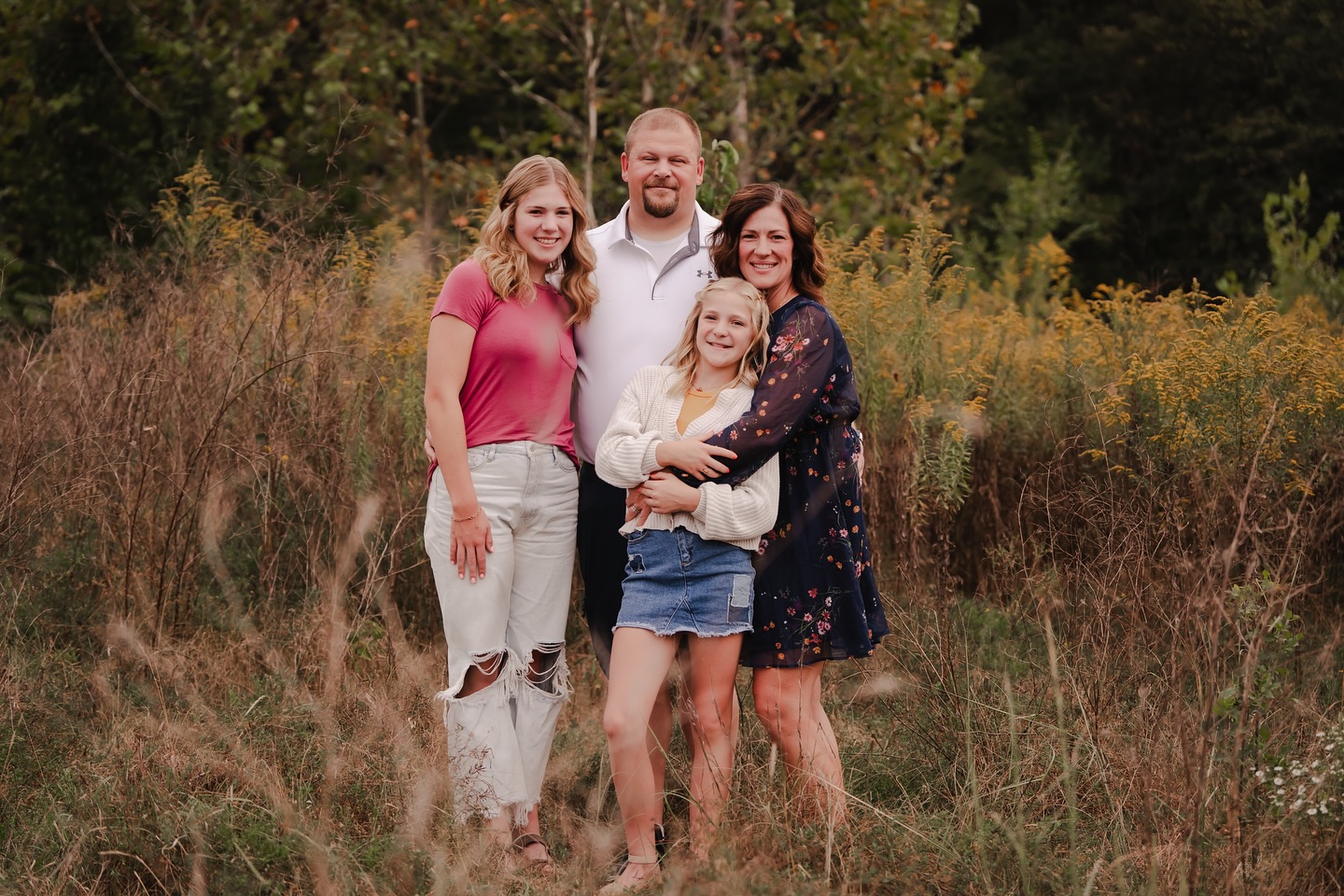 A smiling family of four posing together in a beautiful wildflower field.