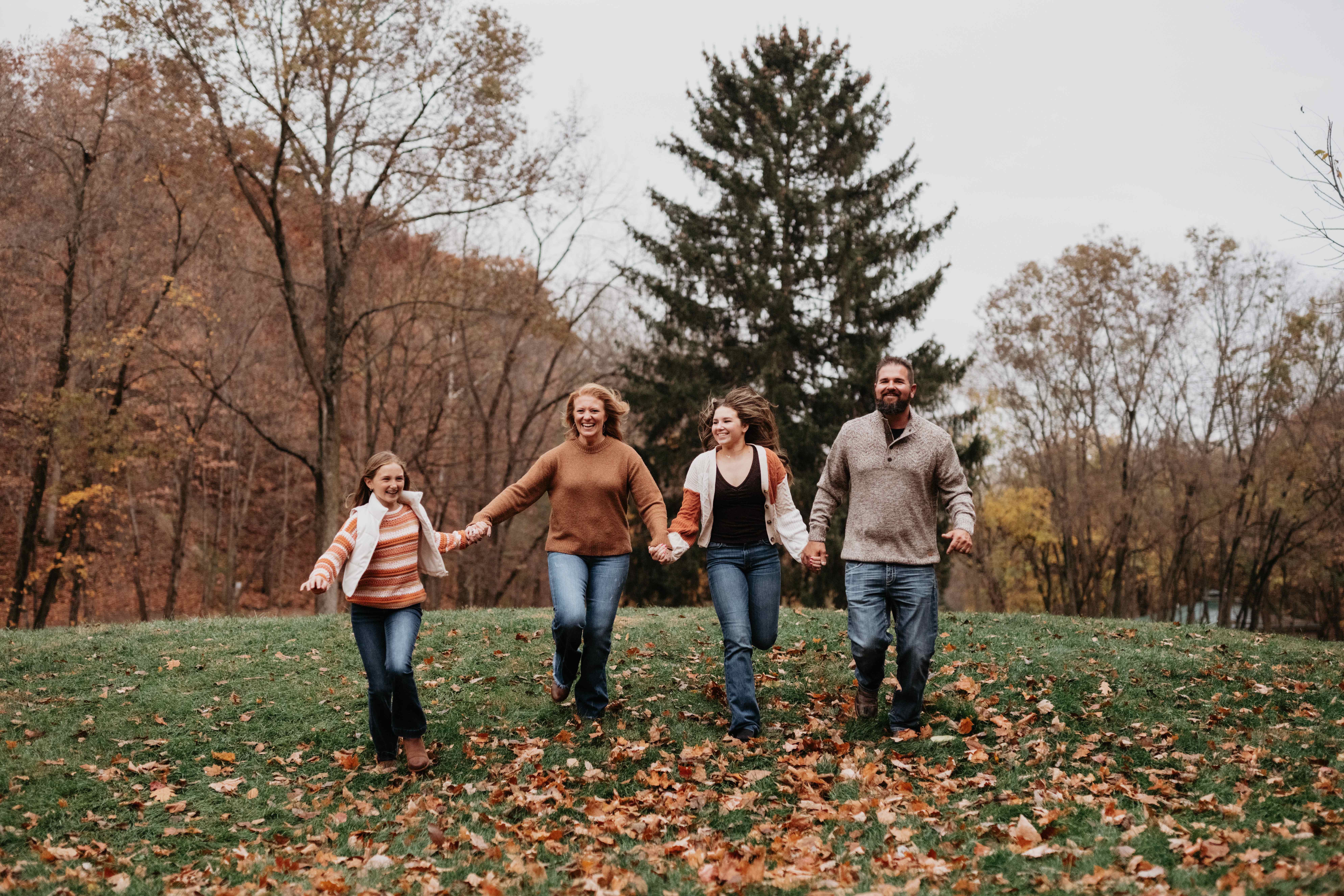 A joyful family of four running hand-in-hand down a grassy hill in the fall.