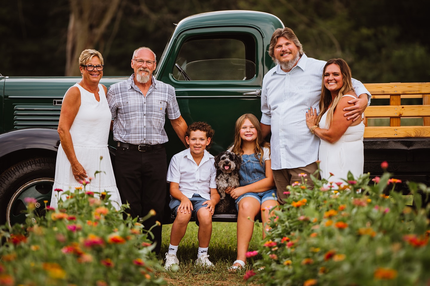 Multi-generational family smiling in front of a vintage green truck and a flower garden.