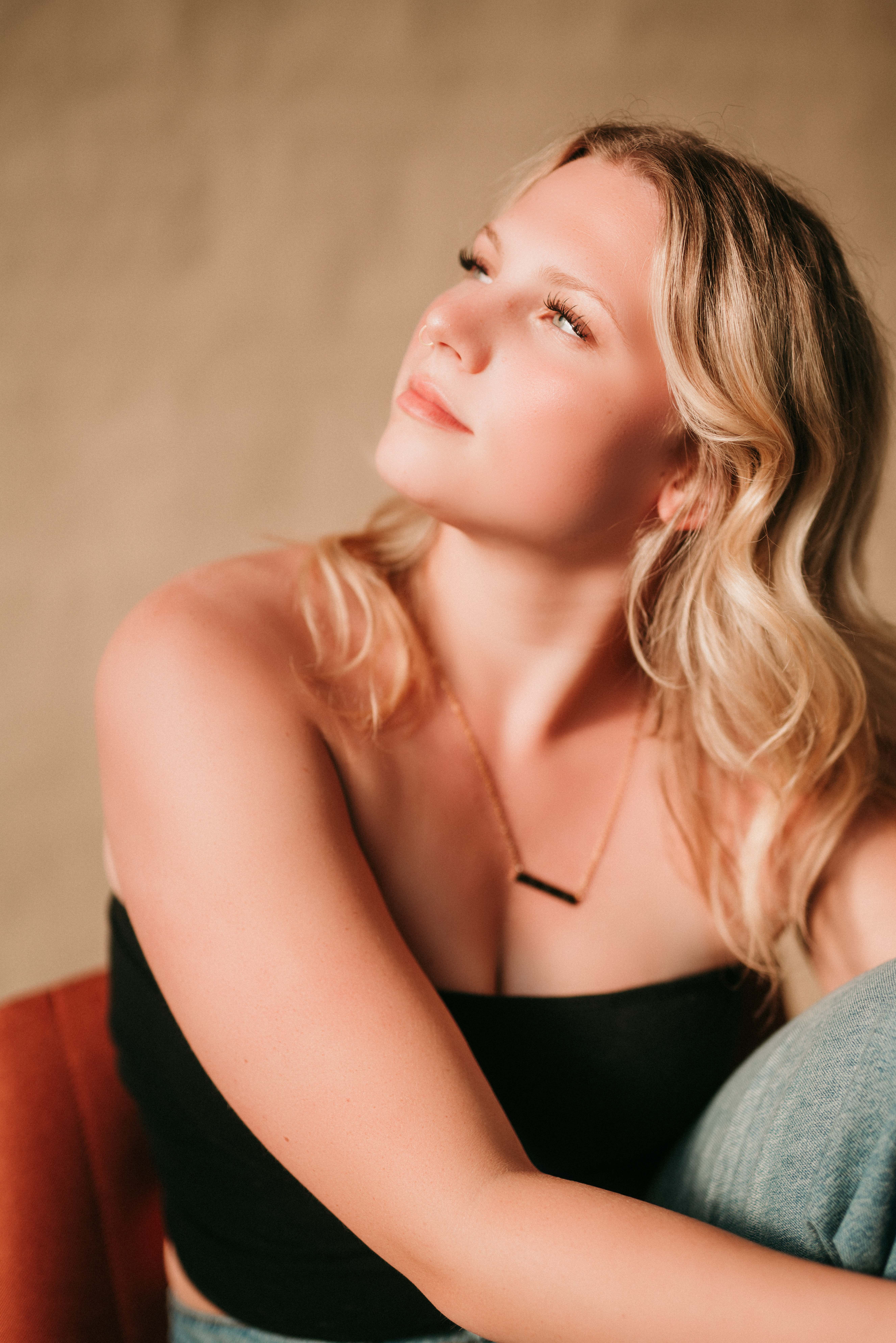 Thoughtful blonde senior in a black top looking upwards in a studio setting.