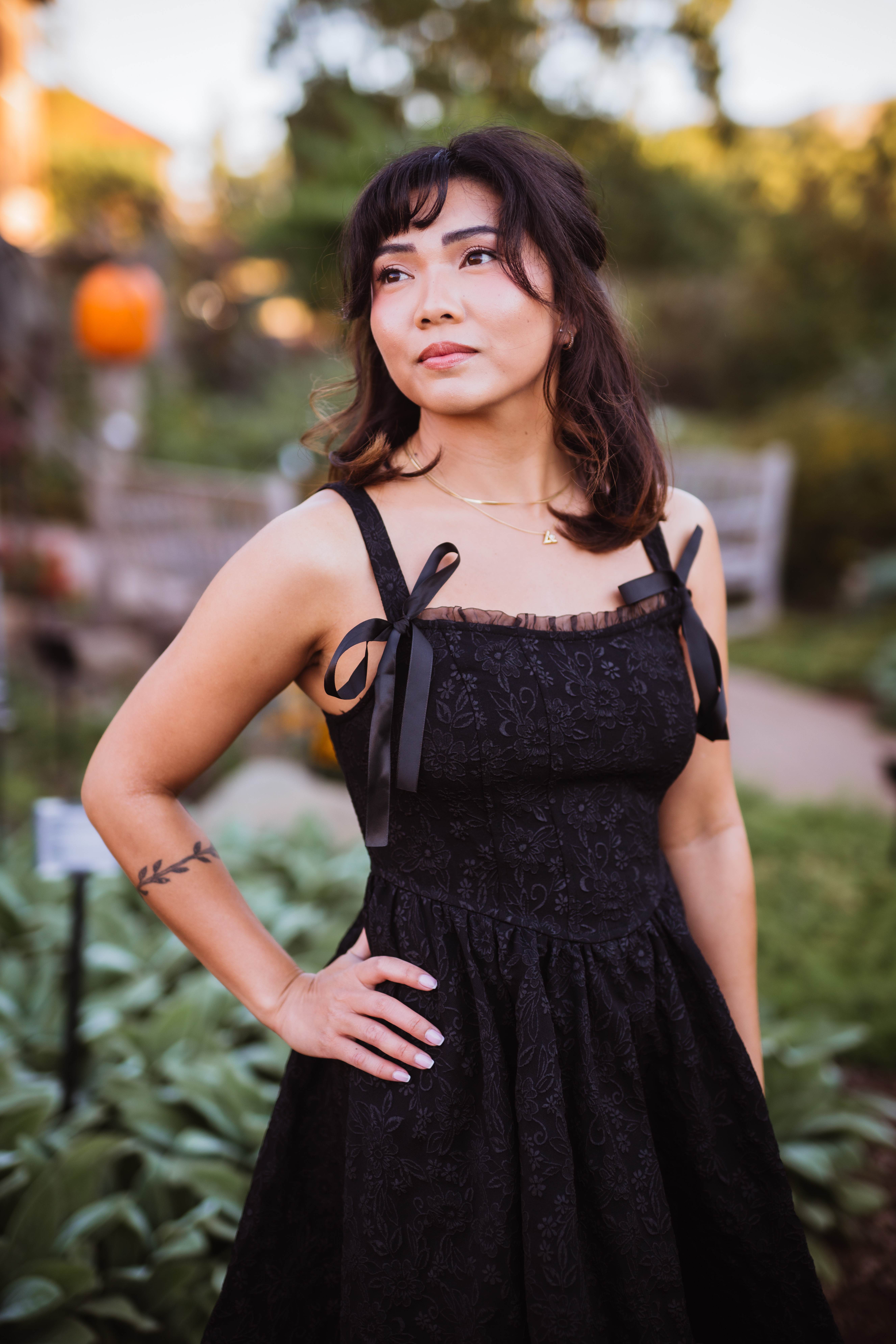 Senior with dark hair in an elegant black dress posing in a garden.
