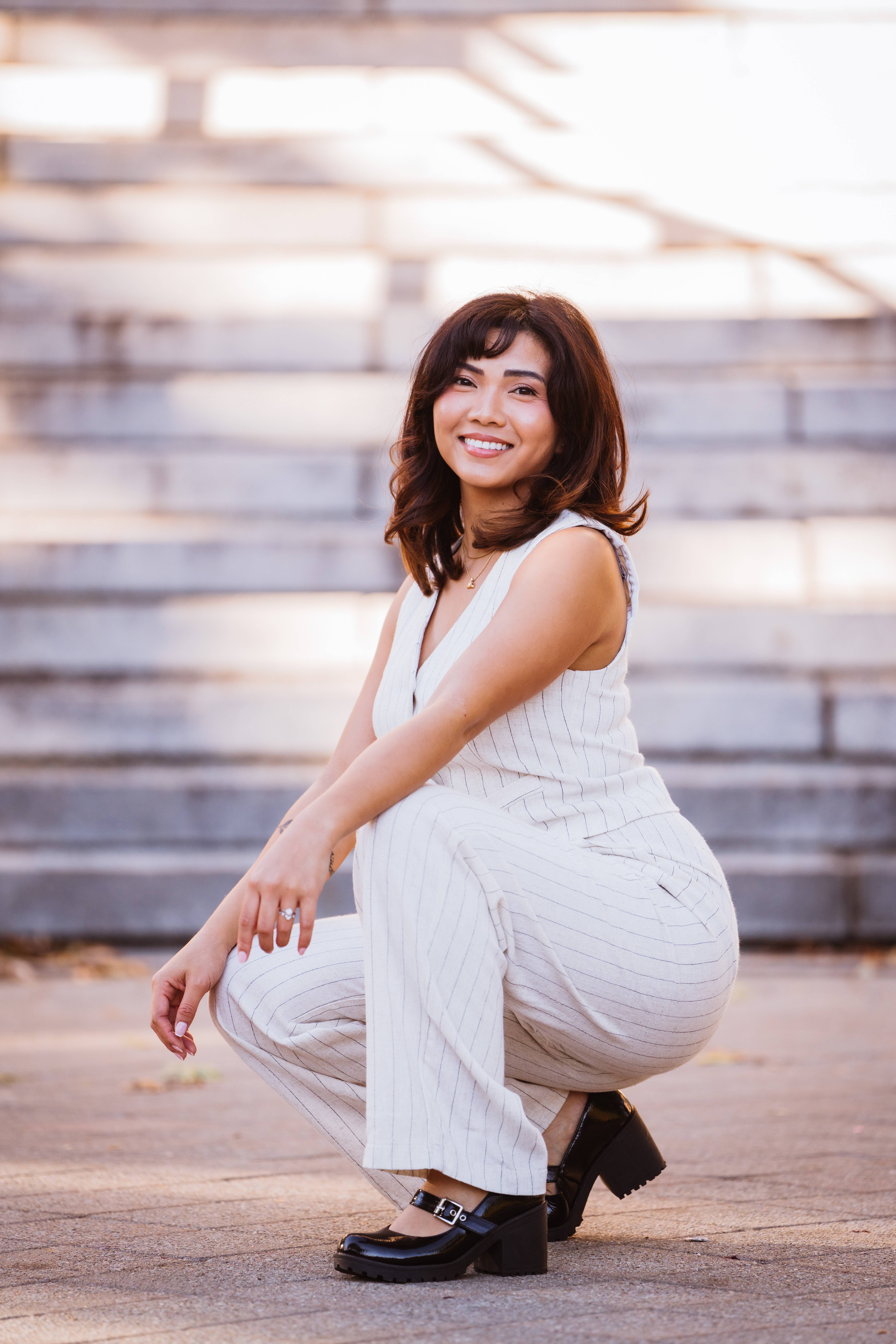 Smiling senior in a white pinstripe suit crouching outdoors with steps in the background.