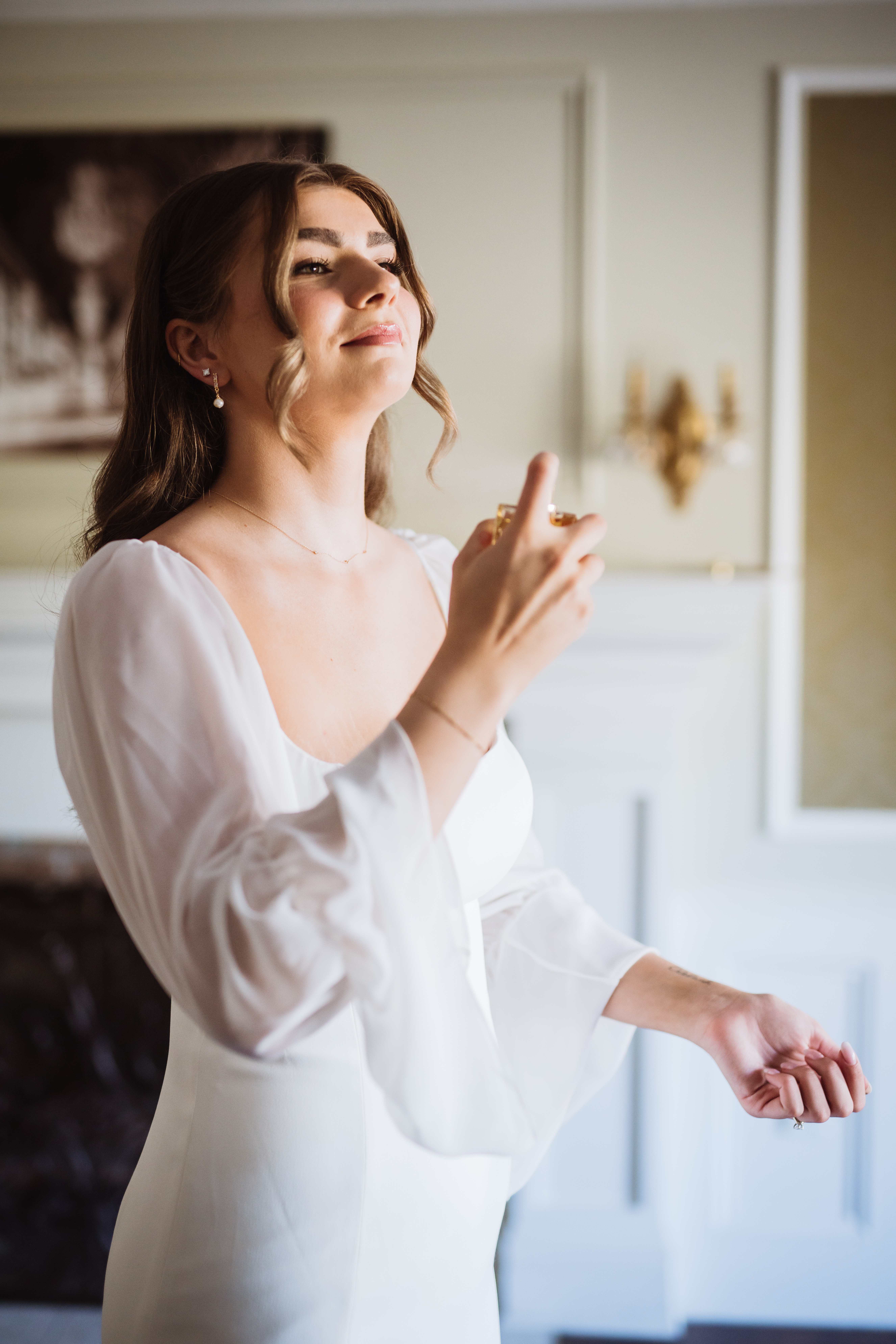 Bride smiling while spraying perfume as she gets ready for her wedding.