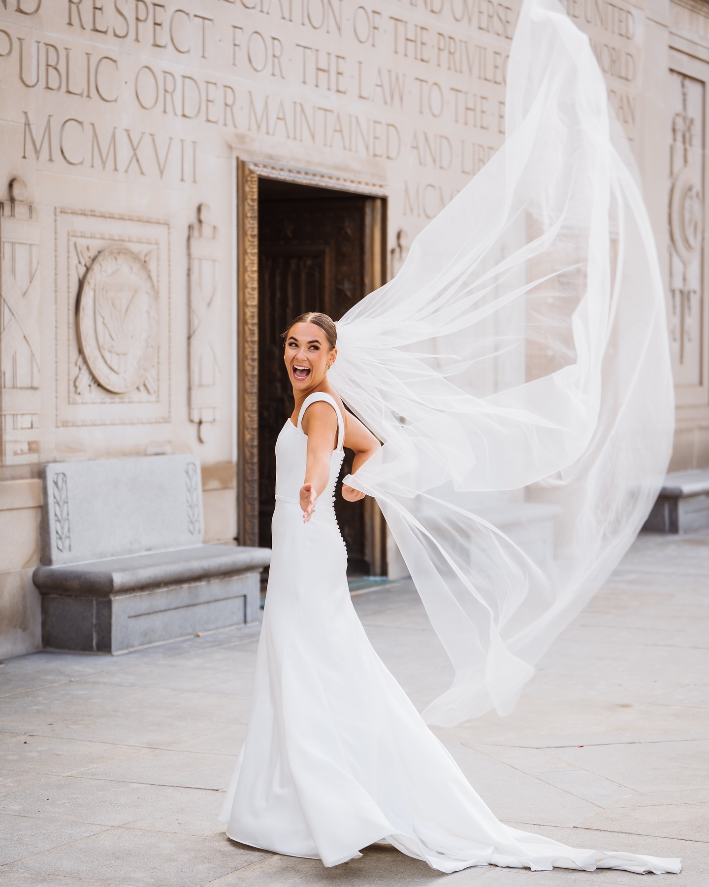 Joyful bride looking back with her long veil flying in the wind in front of a stone building.