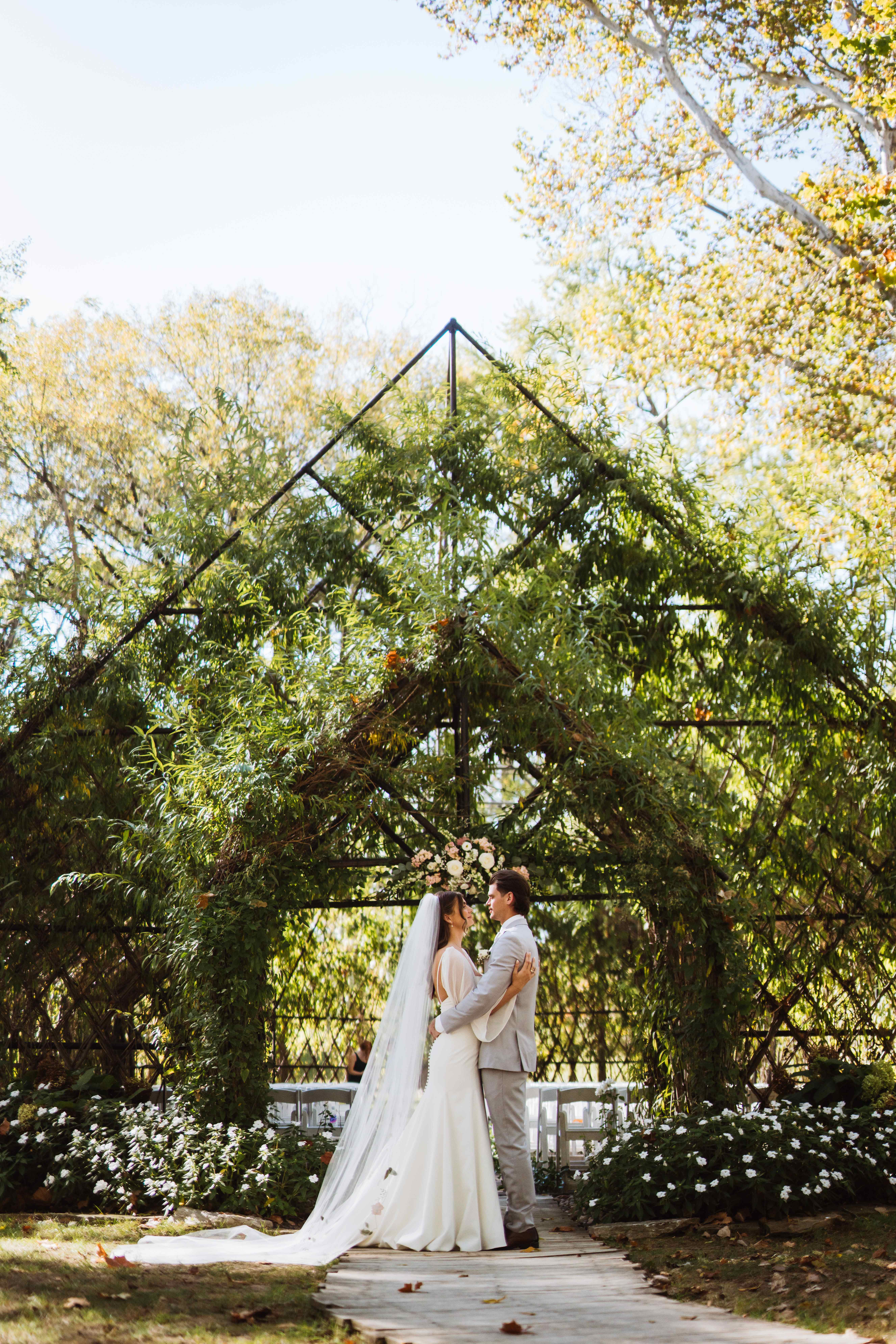 Bride and groom embracing under a beautiful leafy wedding arch outdoors.